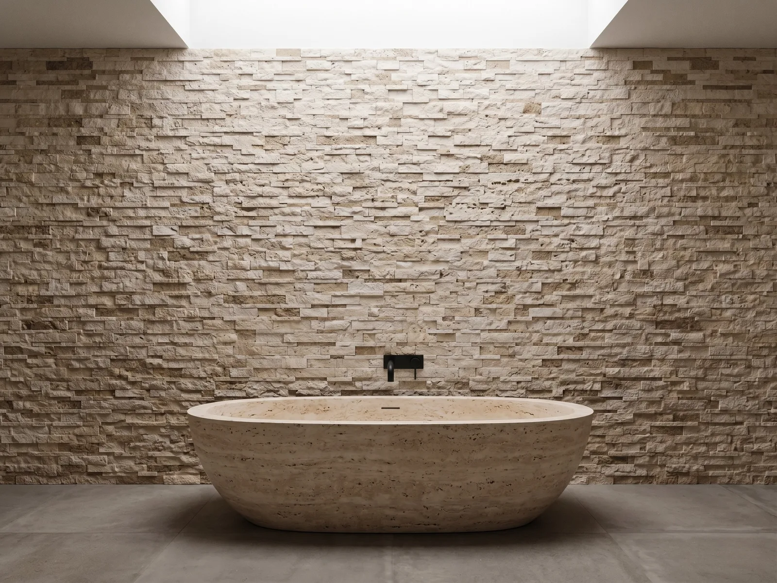 Freestanding oval stone bath centred against a Light Noce travertine ledger panel wall, with a slot skylight above and a dark wall-mounted spout.