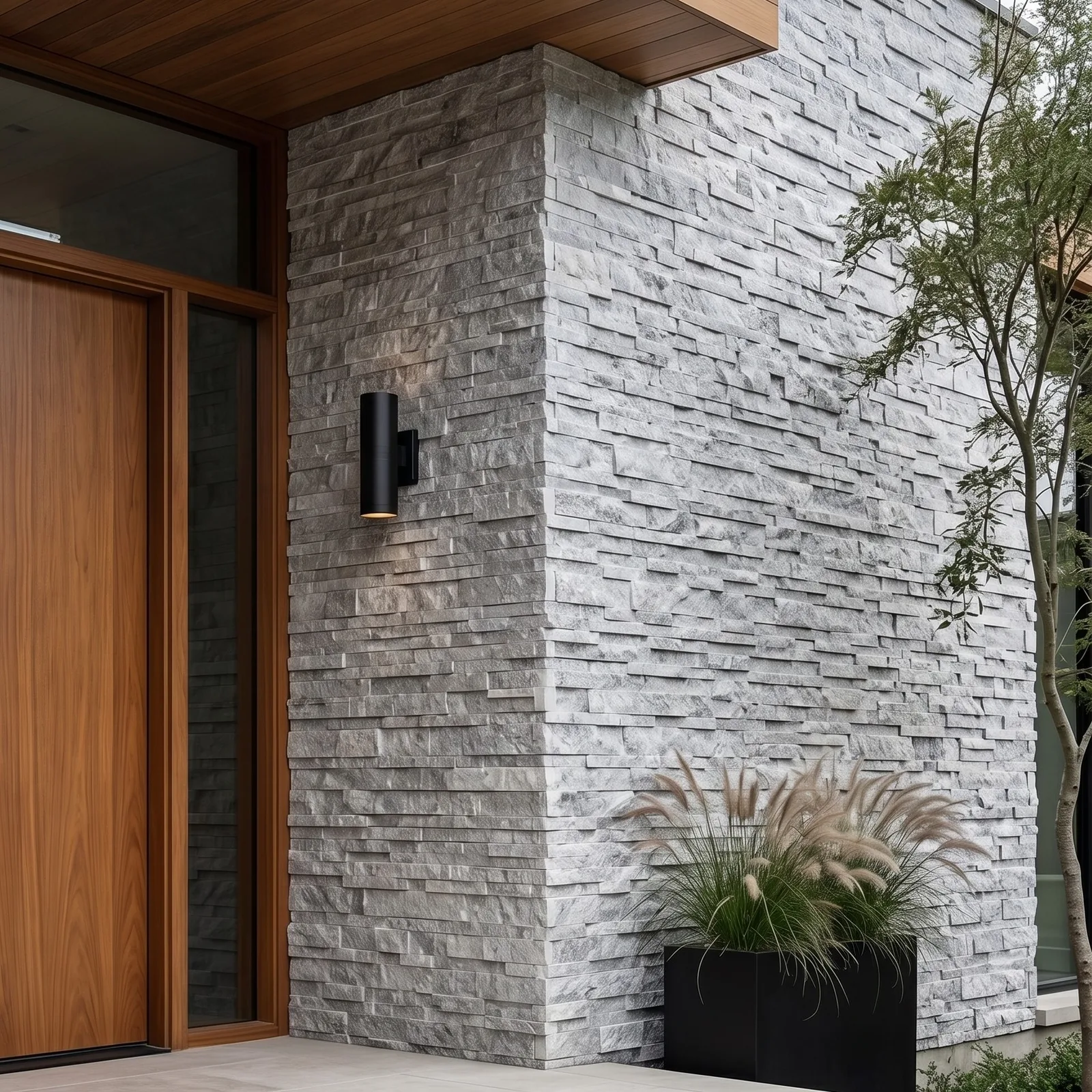 Entrance elevation clad in Tundra Grey marble ledger panel, a timber door and deep soffit above, with planting at the base of the pale grey stone.