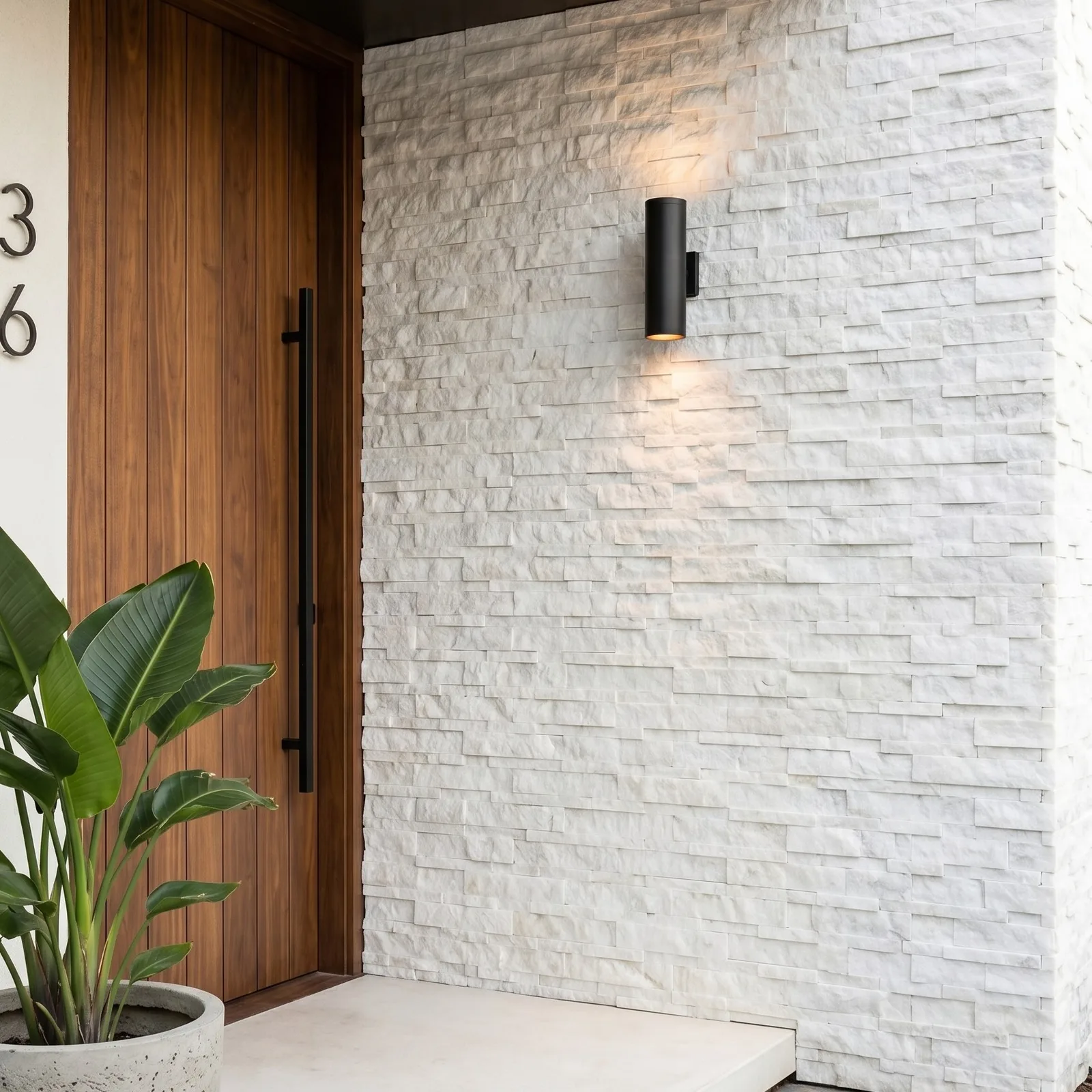 Entrance elevation in white marble ledger panel, a timber front door and house number set against the split-face stone with a black wall light above.
