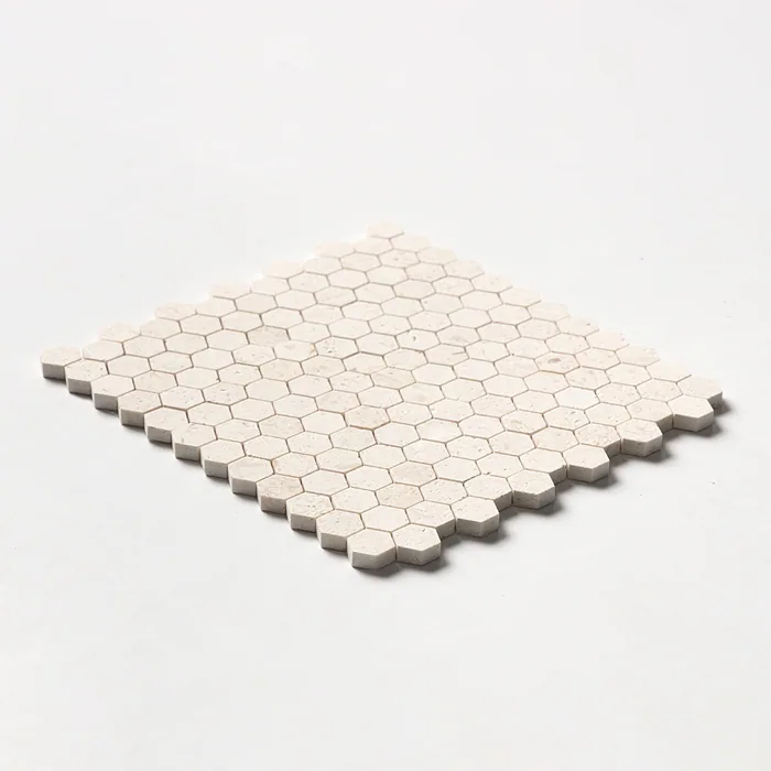 Small one-inch limestone hexagons in pale sand, the sheet tilted low so the honeycomb edge steps away across a white ground.