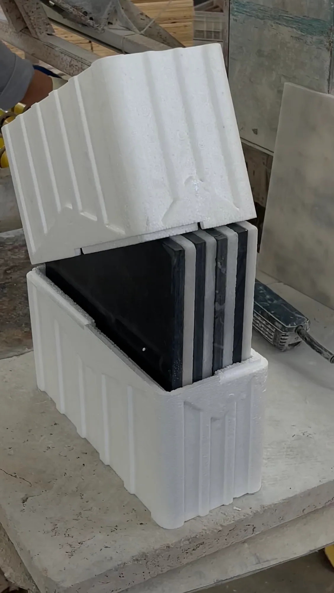 Polished black marble tiles slotted upright into a moulded polystyrene transport case with its lid lifted clear.